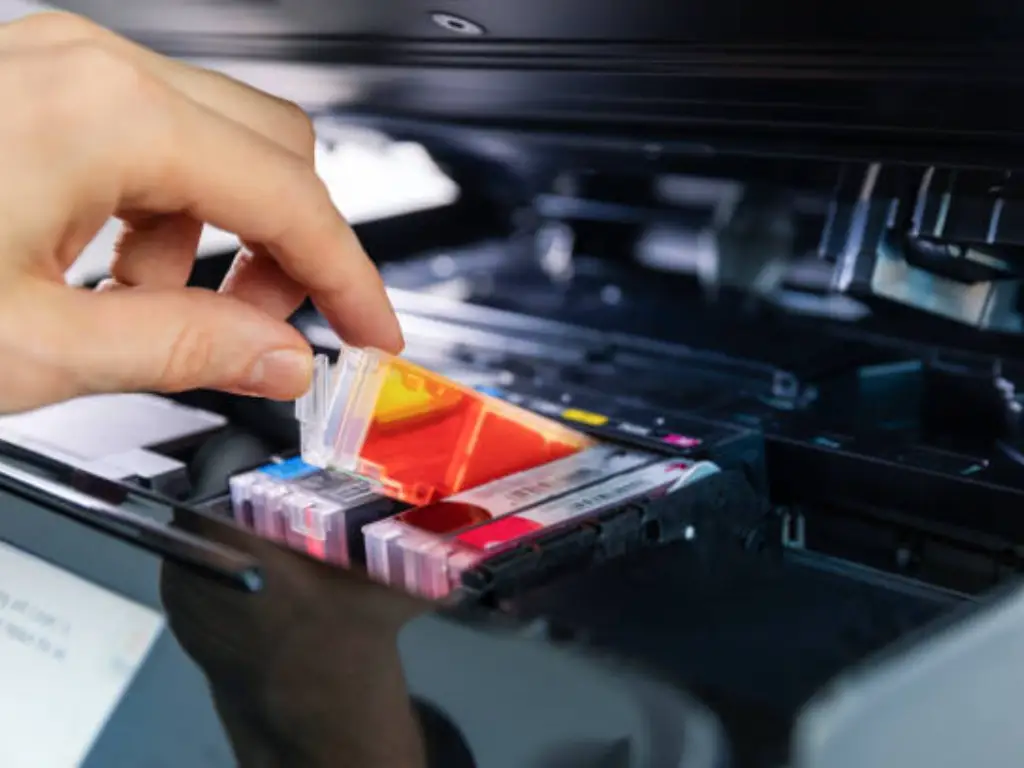 Hand inserting a colour ink cartridge into a business printer. Stock photography for illustrative context, not a catalogue or official brand photograph.
