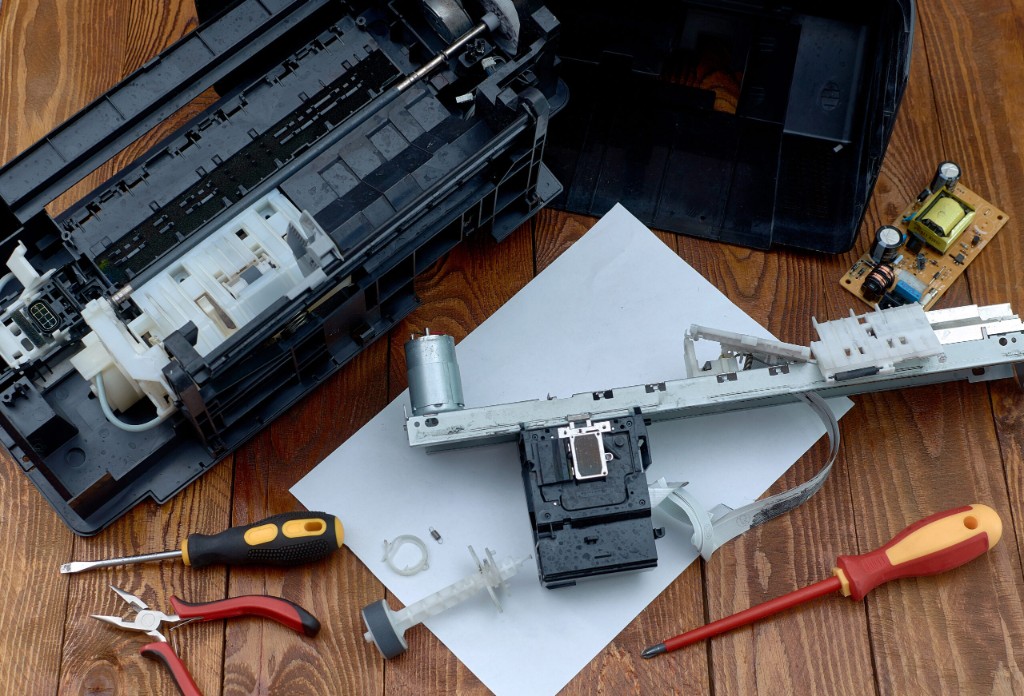 Disassembled printer parts and tools on a workbench. Stock photography for illustrative context, not a catalogue or official brand photograph.